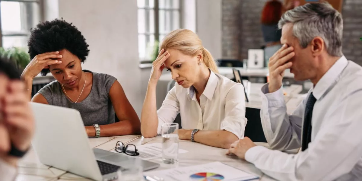 Tres personas en una reunión de trabajo muestran signos de preocupación y cansancio frente a una computadora, reflejando desmotivación y bajo rendimiento laboral. 