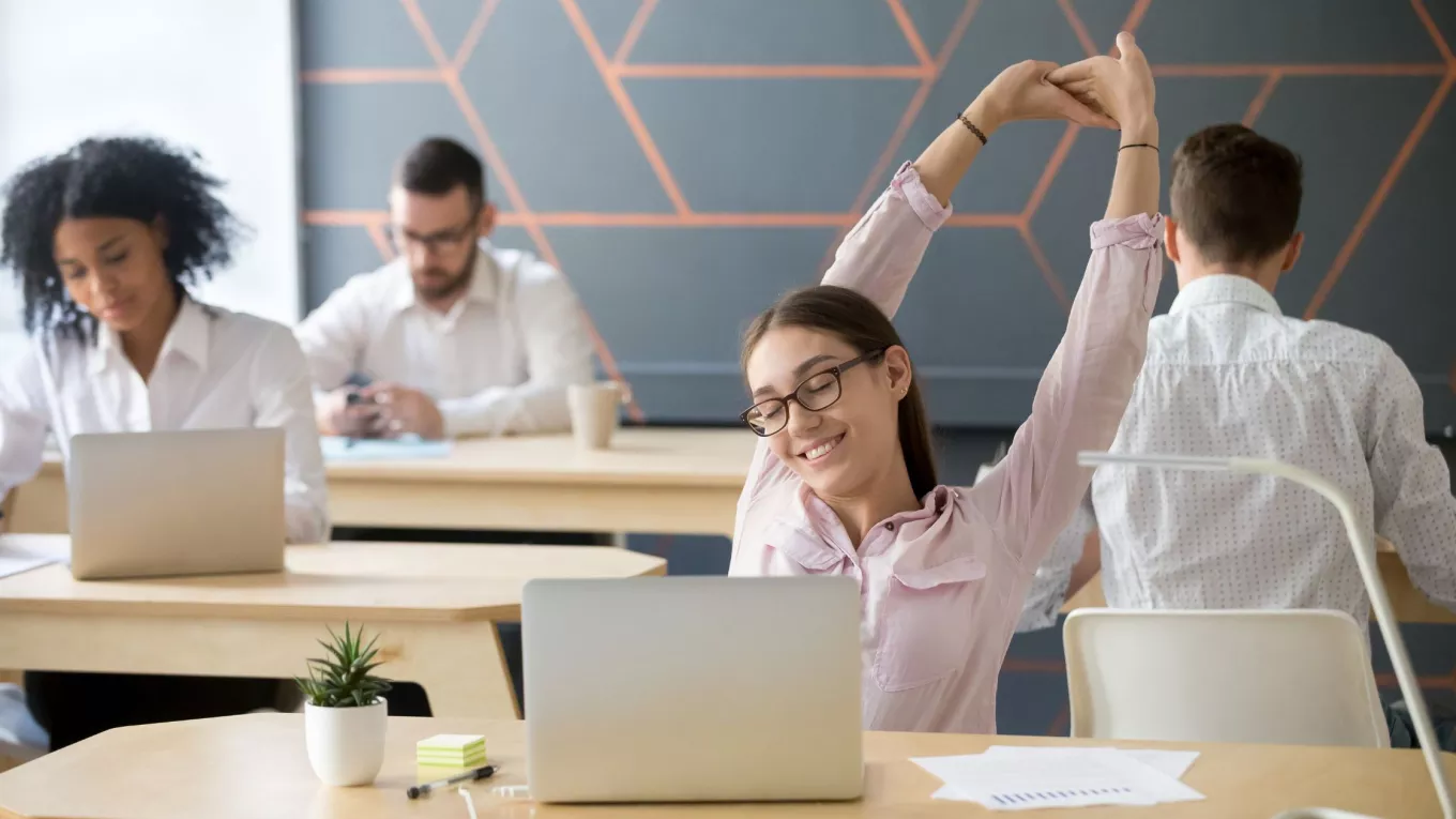 Trabajadora realiza una pausa activa y estira los brazos para cuidar su salud laboral en la oficina.