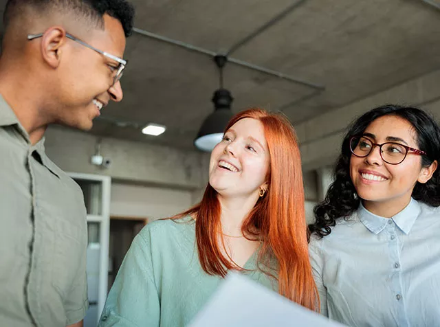 Tres compañeros de trabajo de diferentes etnias conversan animadamente. 