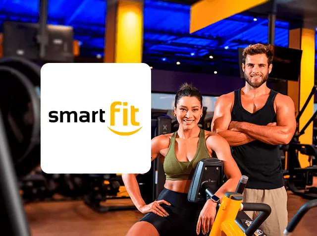 Logo de Smart Fit junto a dos personas en gimnasio, entre maquinas de ejercicio
