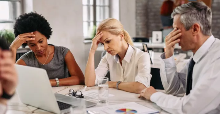 Tres personas en una reunión de trabajo muestran signos de preocupación y cansancio frente a una computadora, reflejando desmotivación y bajo rendimiento laboral.