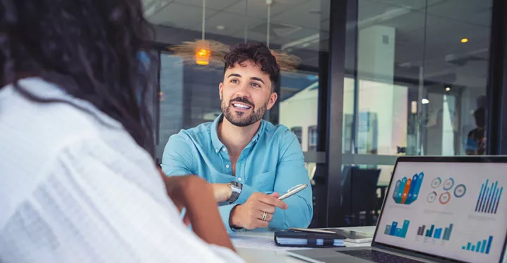 La foto muestra a dos personas conversando en la oficina.