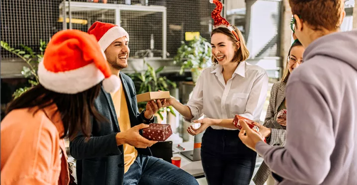 Compañeros de trabajo celebran la Navidad intercambiando regalos en un amigo secreto.