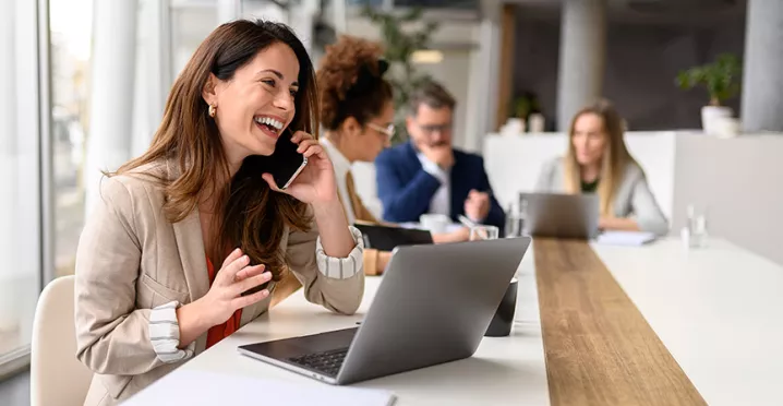 Ejecutiva hablando por teléfono con su equipo de trabajo al fondo