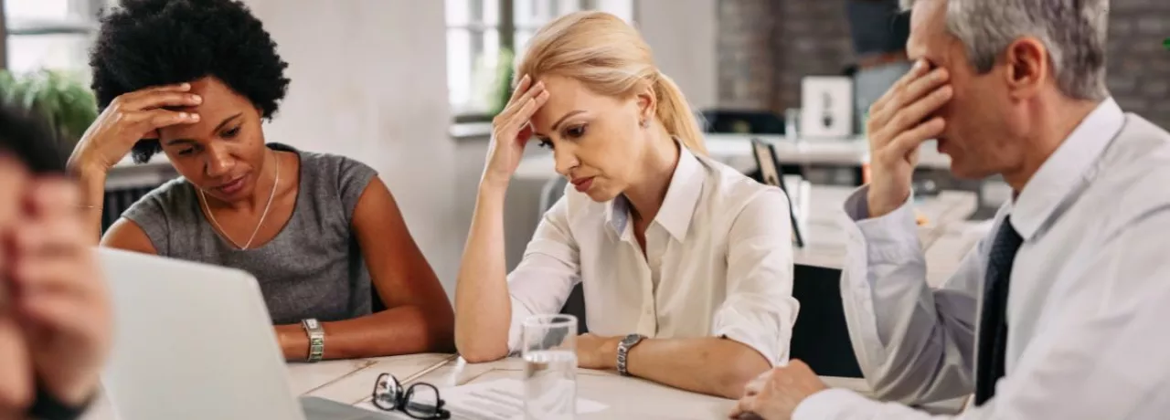 Tres personas en una reunión de trabajo muestran signos de preocupación y cansancio frente a una computadora, reflejando desmotivación y bajo rendimiento laboral.