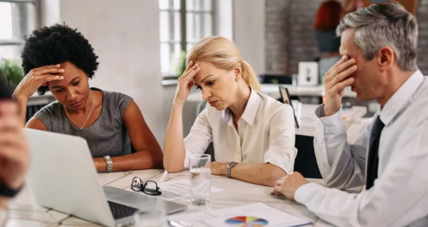 Tres personas en una reunión de trabajo muestran signos de preocupación y cansancio frente a una computadora, reflejando desmotivación y bajo rendimiento laboral.