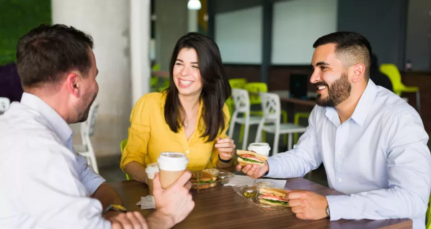 Compañeros de trabajo riendo mientras comparten el almuerzo en la oficina