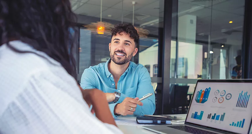 La foto muestra a dos personas conversando en la oficina.