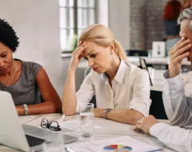 Tres personas en una reunión de trabajo muestran signos de preocupación y cansancio frente a una computadora, reflejando desmotivación y bajo rendimiento laboral.