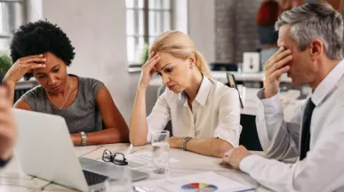 Tres personas en una reunión de trabajo muestran signos de preocupación y cansancio frente a una computadora, reflejando desmotivación y bajo rendimiento laboral.