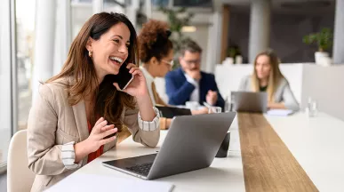 Ejecutiva hablando por teléfono con su equipo de trabajo al fondo
