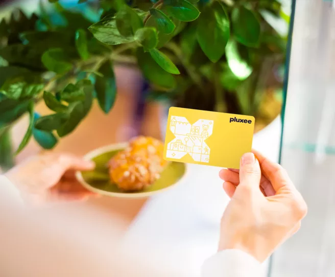 Persona sosteniendo una tarjeta Pluxee Gift Card junto a una mesa con comida y plantas.